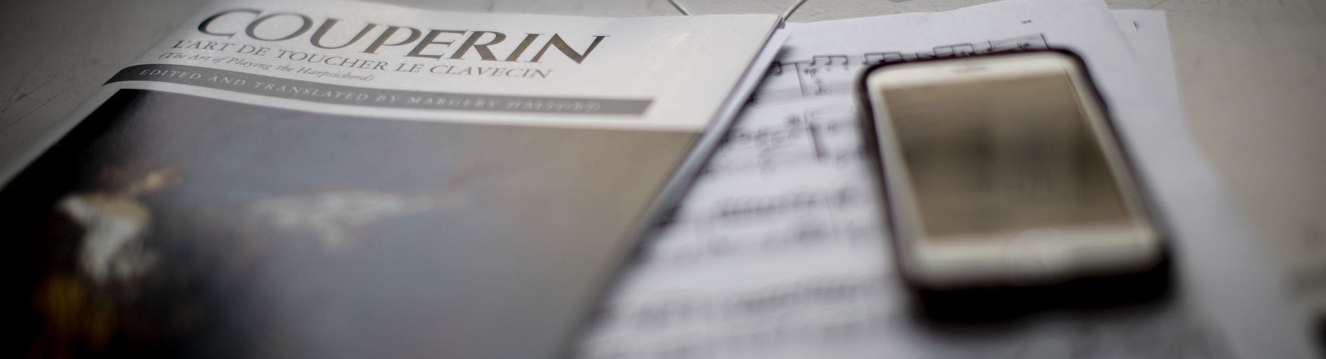 Piano score and other sheet music on a desk with a cell phone.