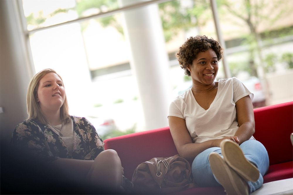 Two students sit next to each other on a couch, engaged in a group discussion.