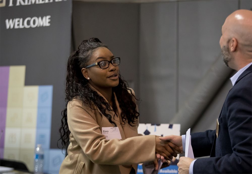 A Temple student shakes hands with a man wearing a suit at a university career fair.