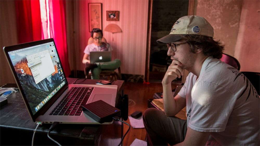 Two students sitting on set working on their laptops.