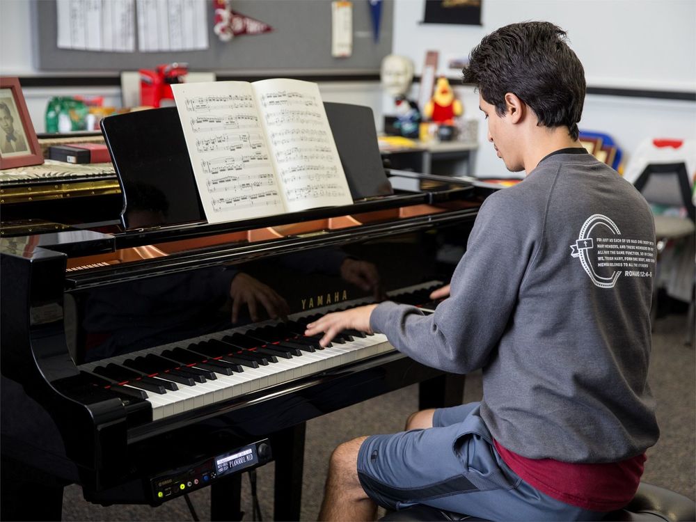 A male student plays a baby grand piano.