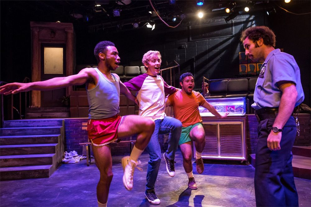 Three guys dance and sing on stage with another actor looking on.