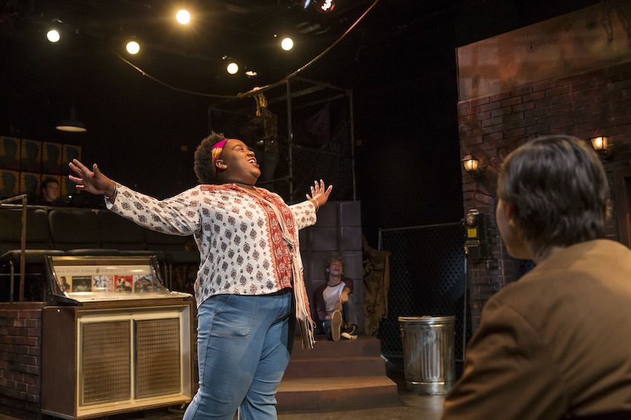 Women with arms outstretched sings on stage.