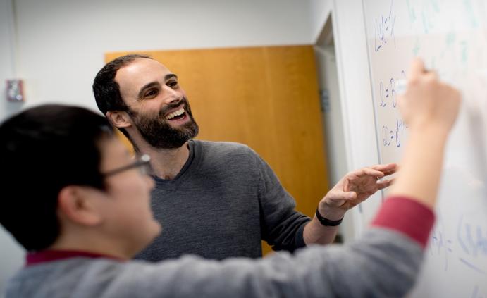 A Temple professor helping a student solve a mathematics equation on a whiteboard in a classroom.