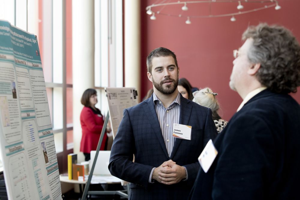 A male student wearing a blazer is in conversation during a professional event.