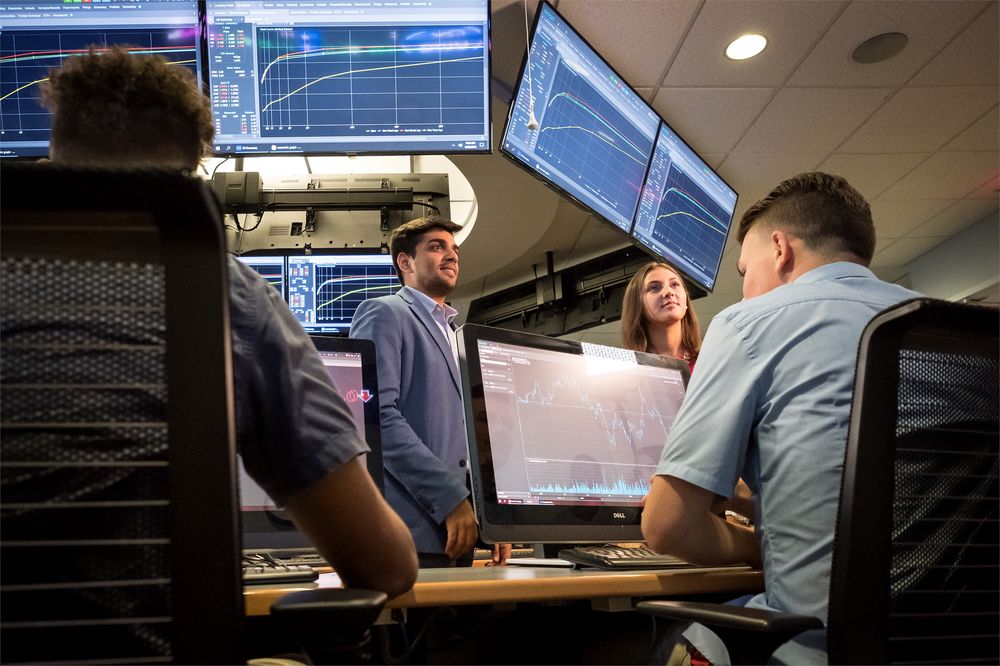 A group of business students analyze financial information, displayed on large screens.