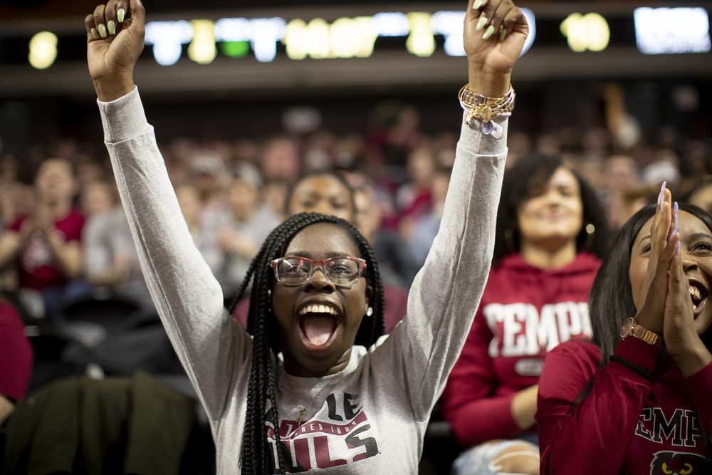 Female student in the crowd at a Temple basketball game has her arms outstretched over her head in glee.