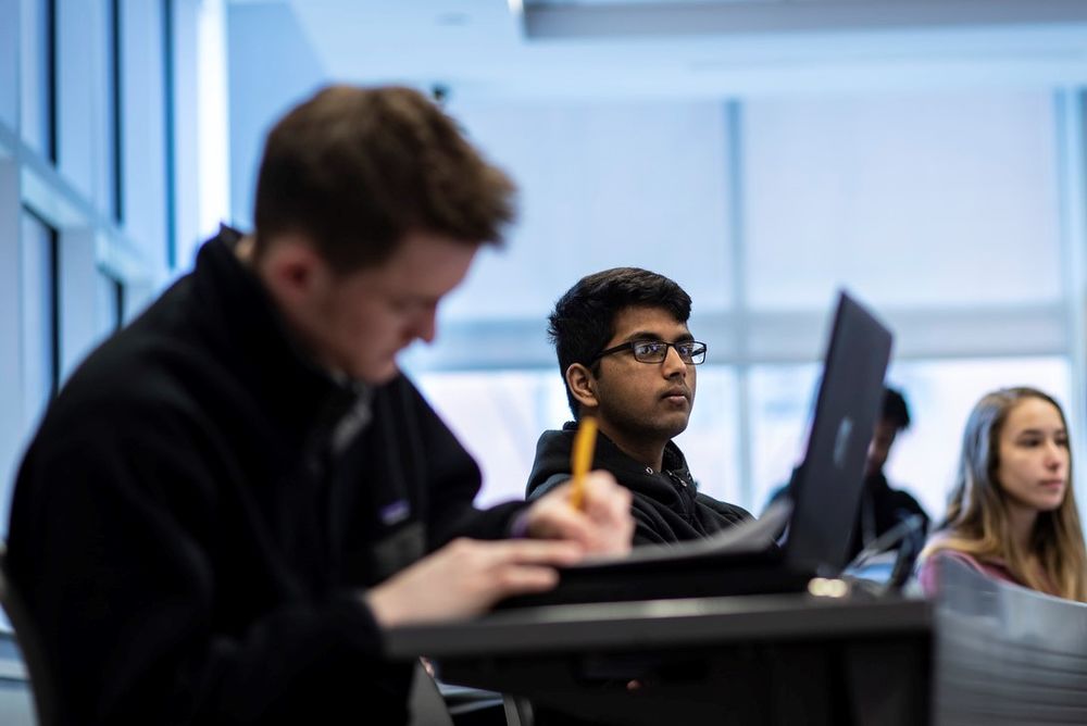 Students sitting in a classroom listening and taking notes.