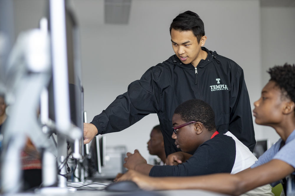 CST student instructs secondary school students on desktop computer. 