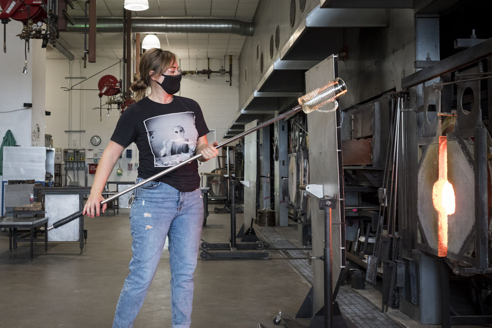 student inserting glass blowing instrument into the kiln. 