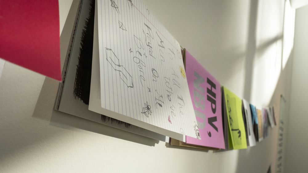 Handmade books hang sideways on a string against a white wall.