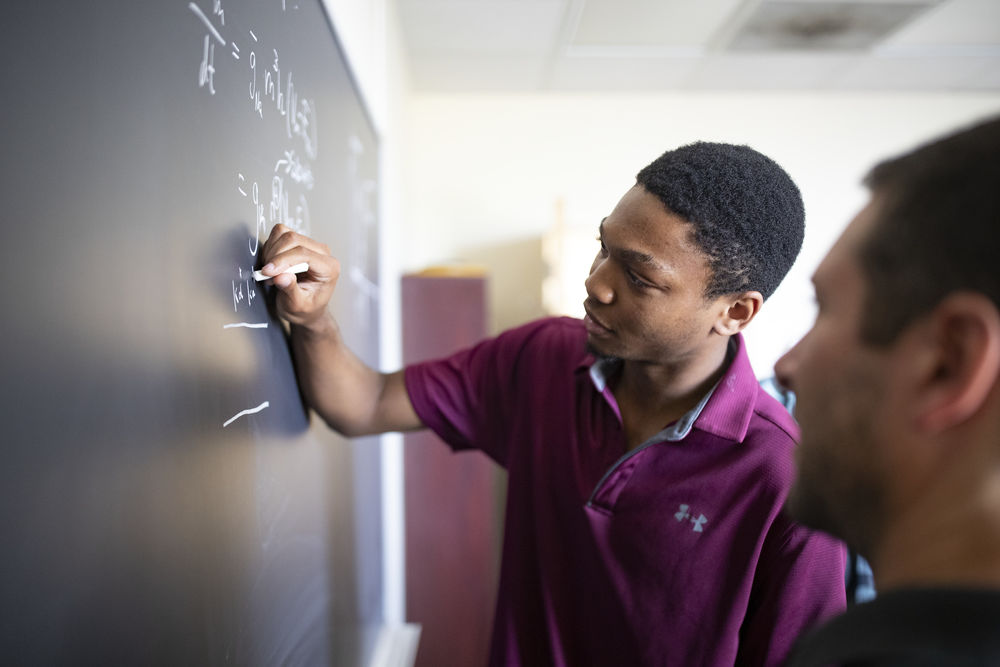 student and professor working through a problem on a chalkboard.