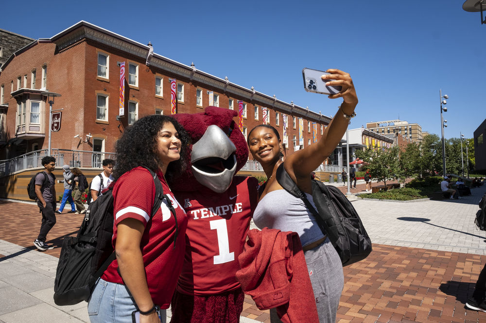 Two Temple students taking a selfie with Hooter, Temple's Owl mascot.