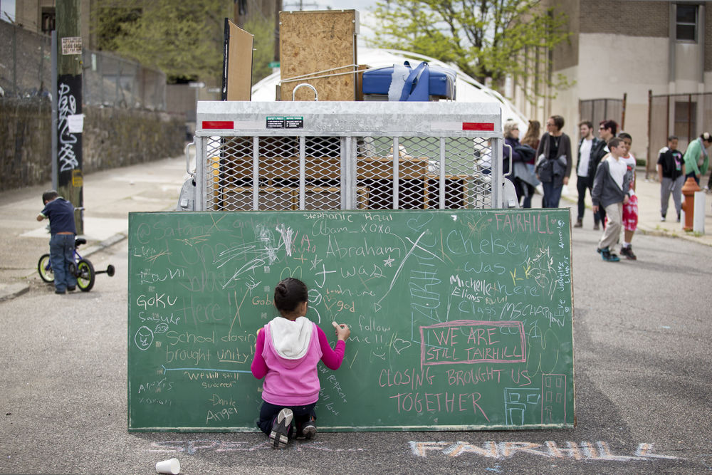 An image of a child writing on a chalkboard in a busy street