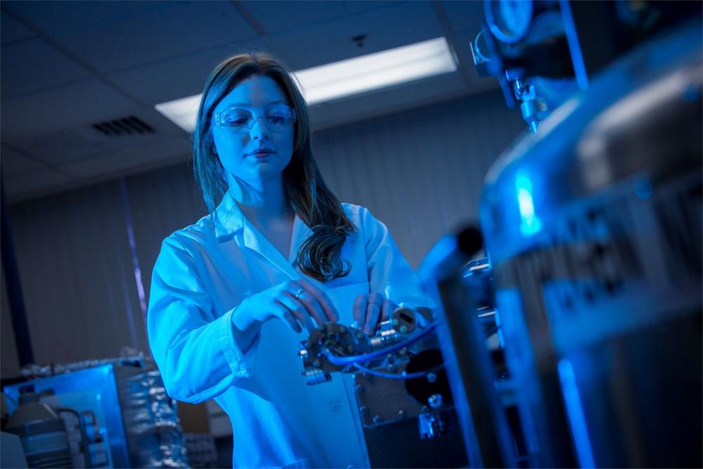 Biochemistry student wearing a lab coat and safety goggles adjusting a machine in the lab