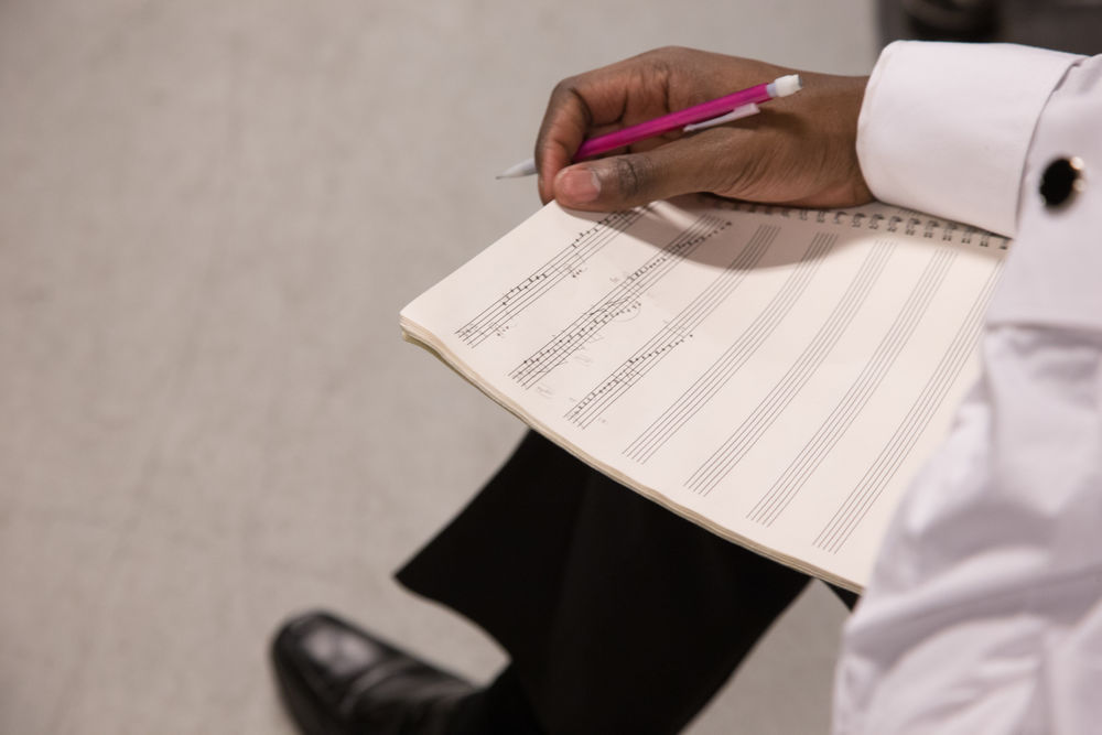 A student with a pencil in hand and sheet music in their lap.