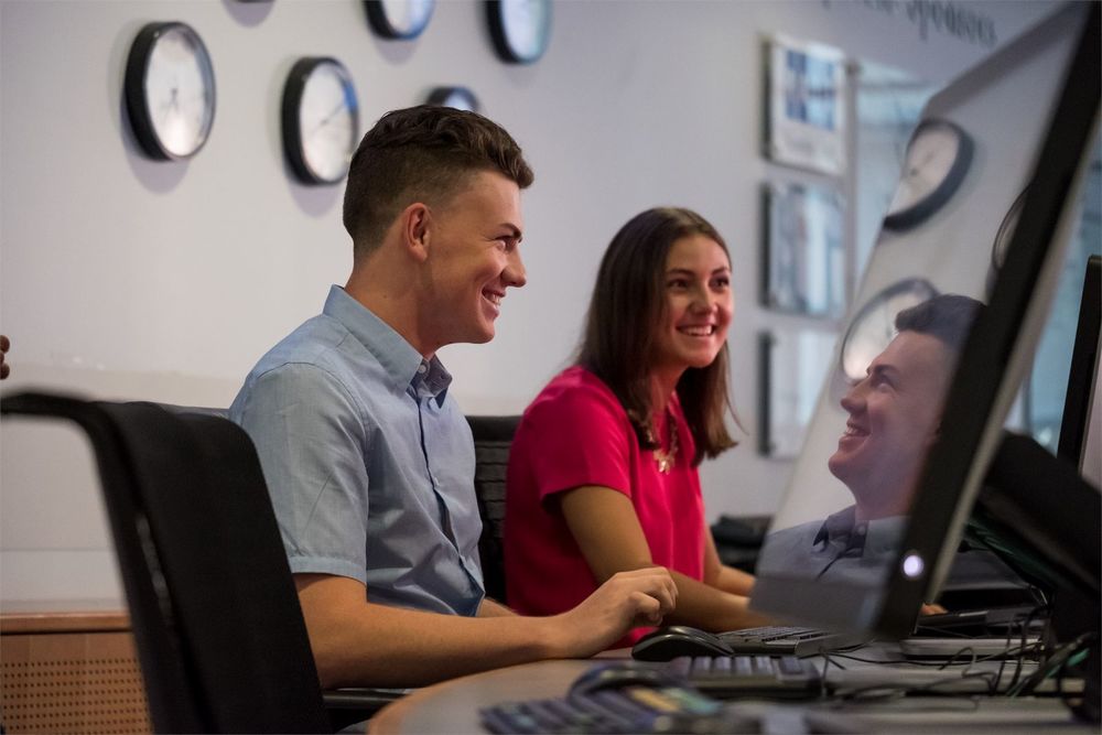 Fox students discuss homework while working at a computer station.