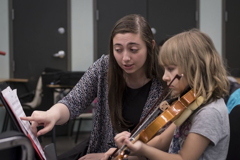 A Temple music student works with an elementary school student during a violin lesson.