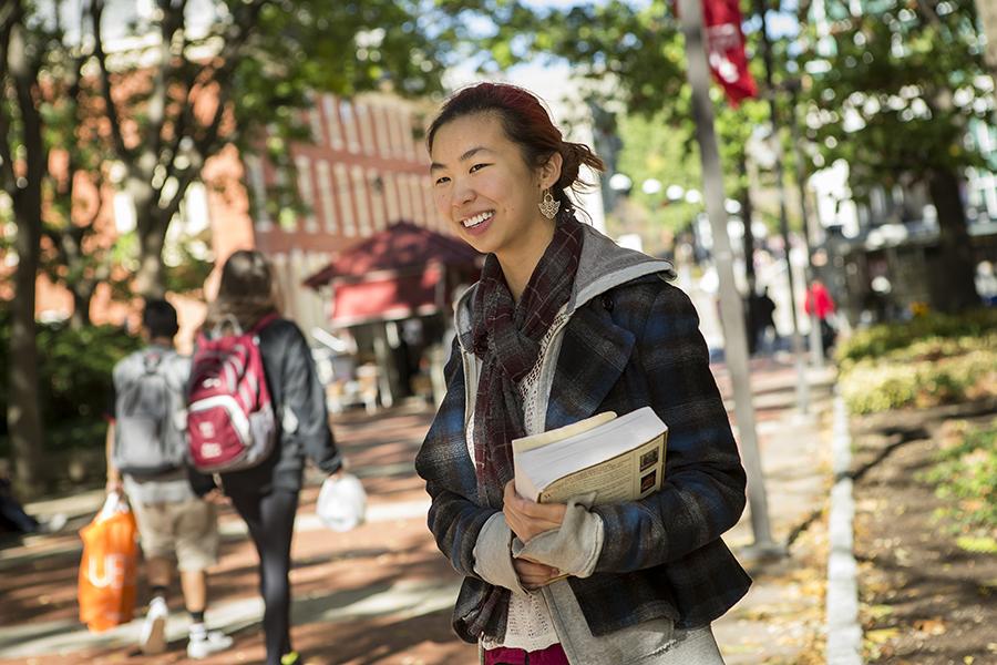 Student holding books standing on university campus path