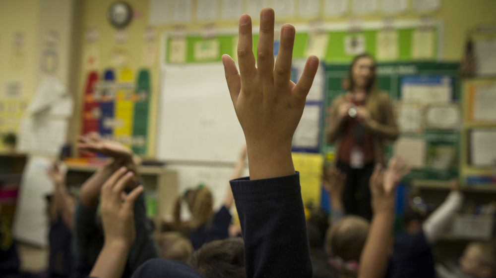 An image of students raising their hand in class